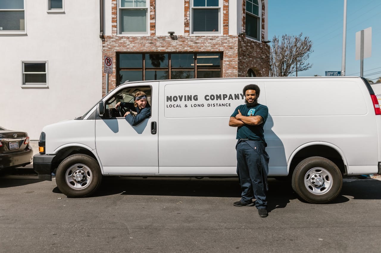 Two men from a moving company stand by their company van on a city street, ready for a job.